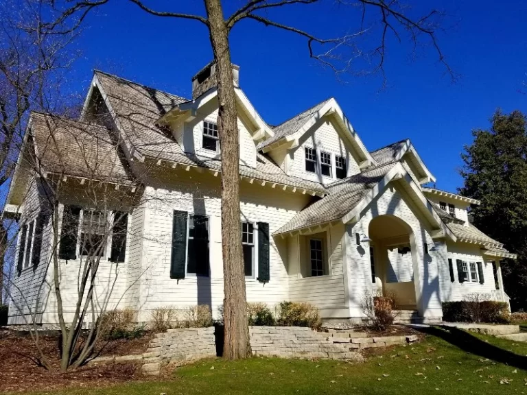 white house with black shudders and bushes before roof cleaning