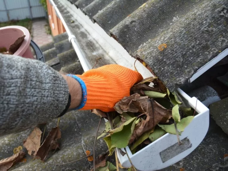 Demarks professional with orange gloves cleaning gutter