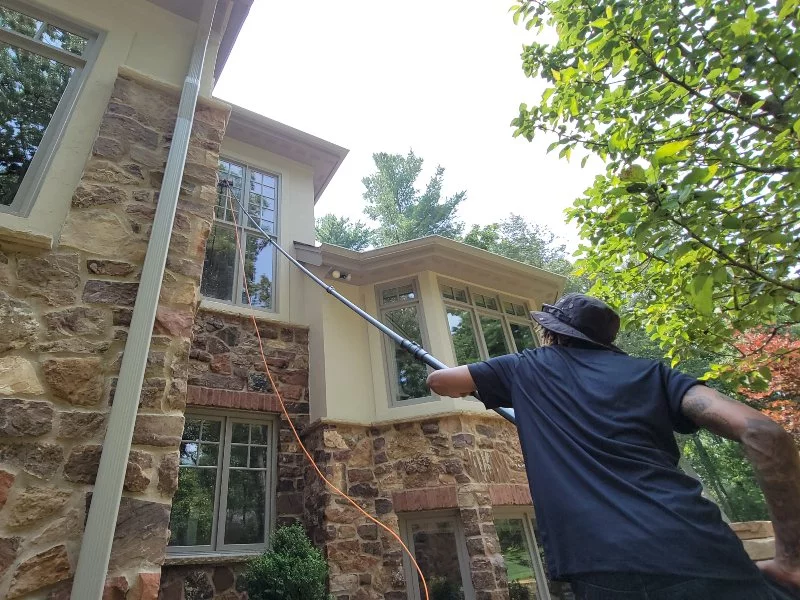 Demarks professional cleaning windows on brick house with beige siding