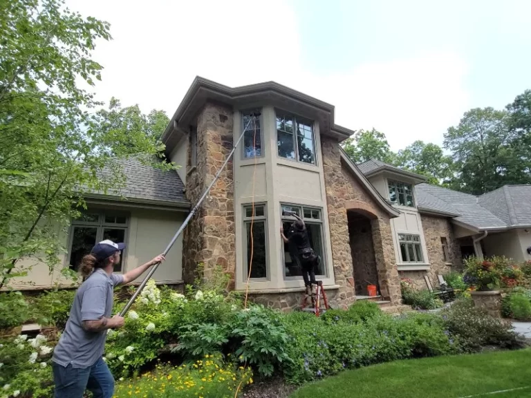 Demarks cleaning professionals cleaning windows on brick house with brown siding
